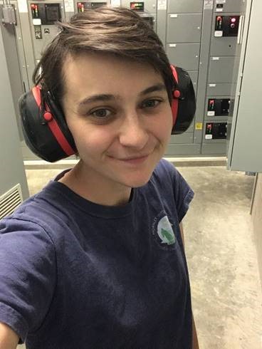 A young woman wearing a blue t-shirt and protective earmuffs.
