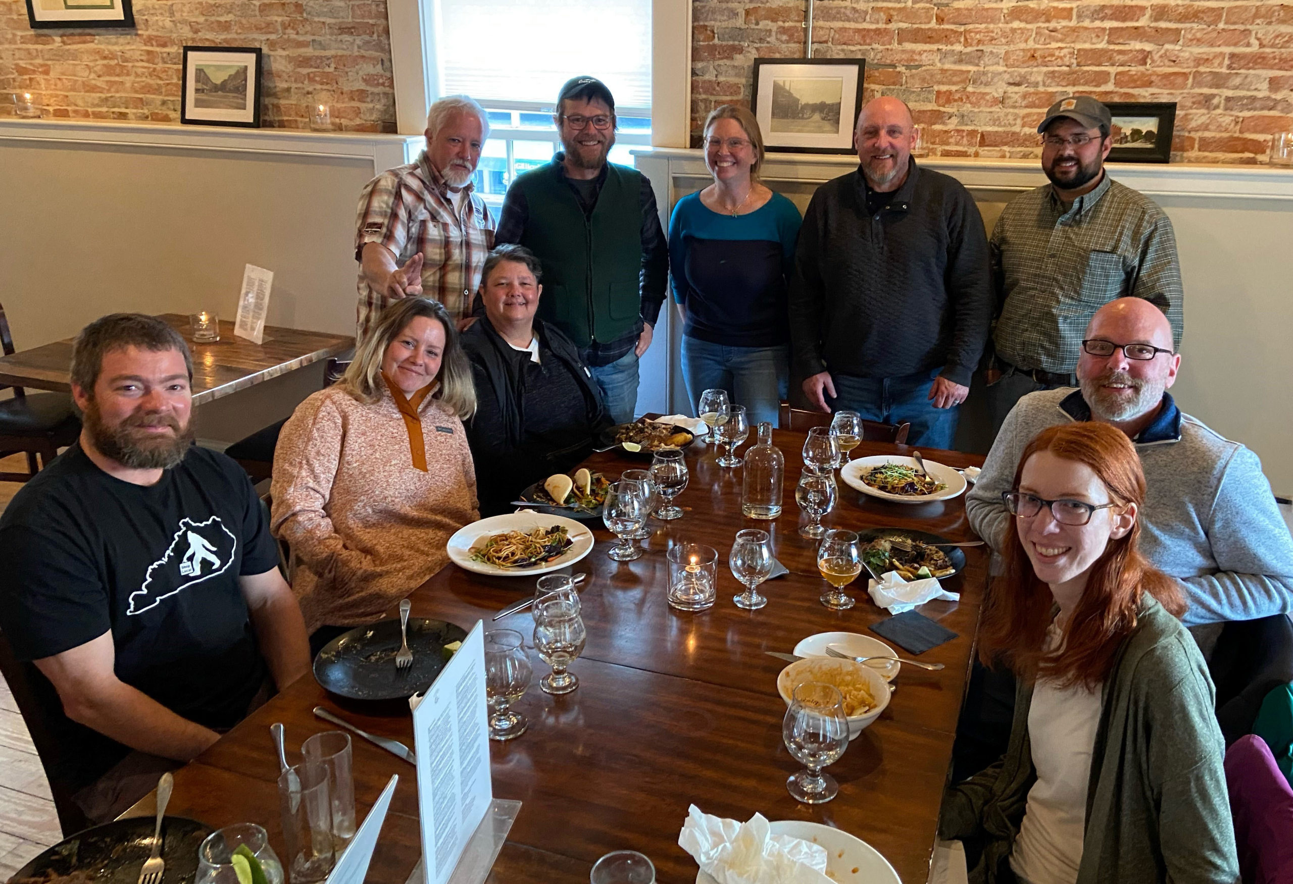 10 people sit and stand around a table