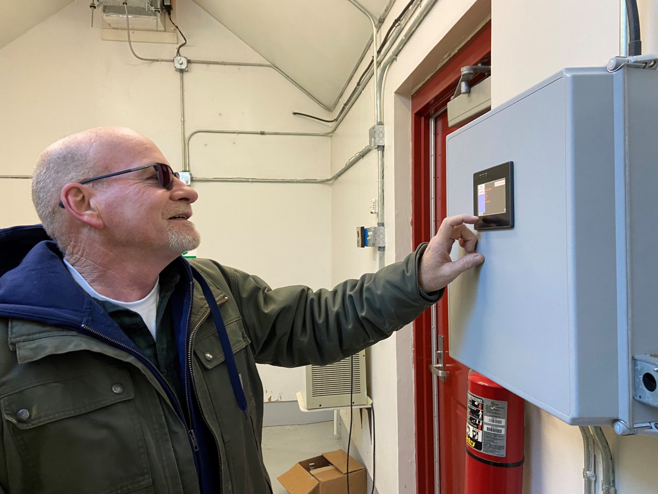 A man points at the electronic display of a box mounted on a wall.