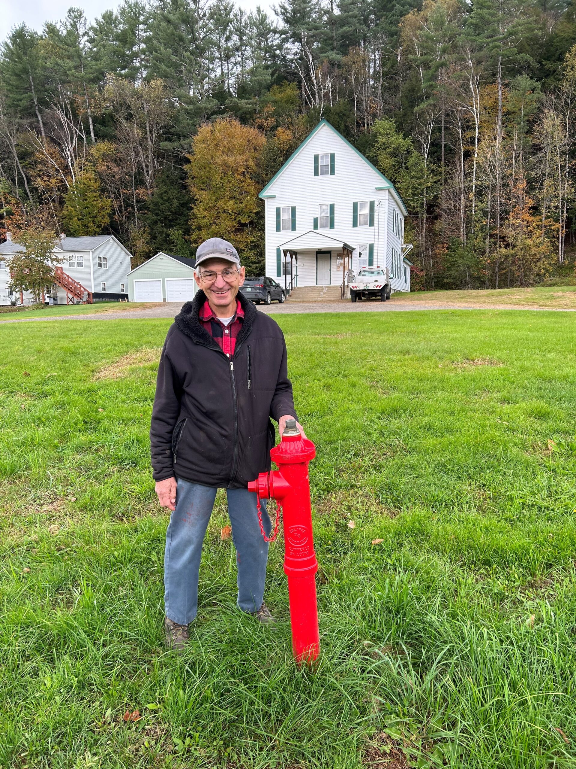 A man stands on a lawn next to a red hydrant