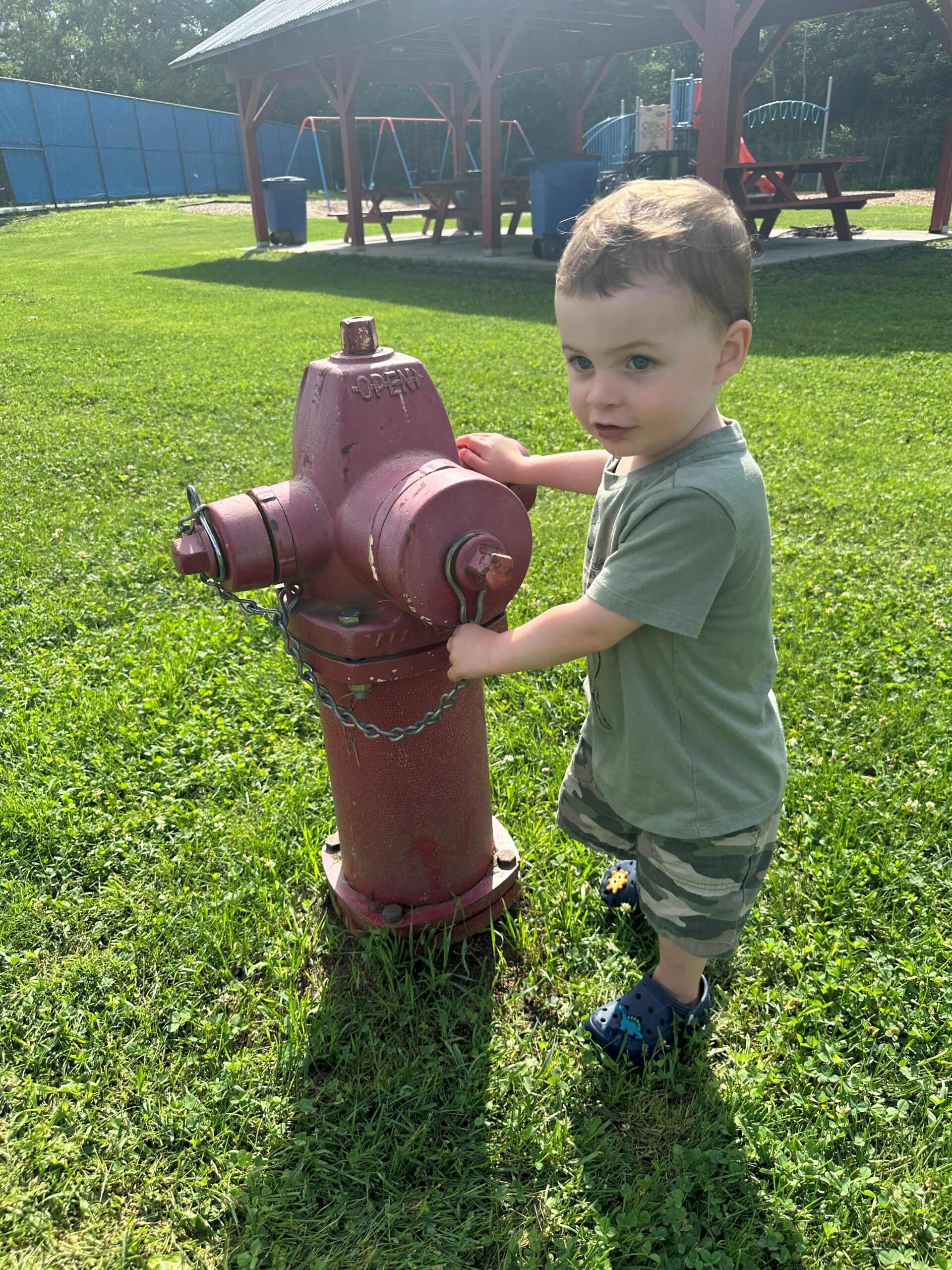 A small boy stands next to a red fire hydrant.