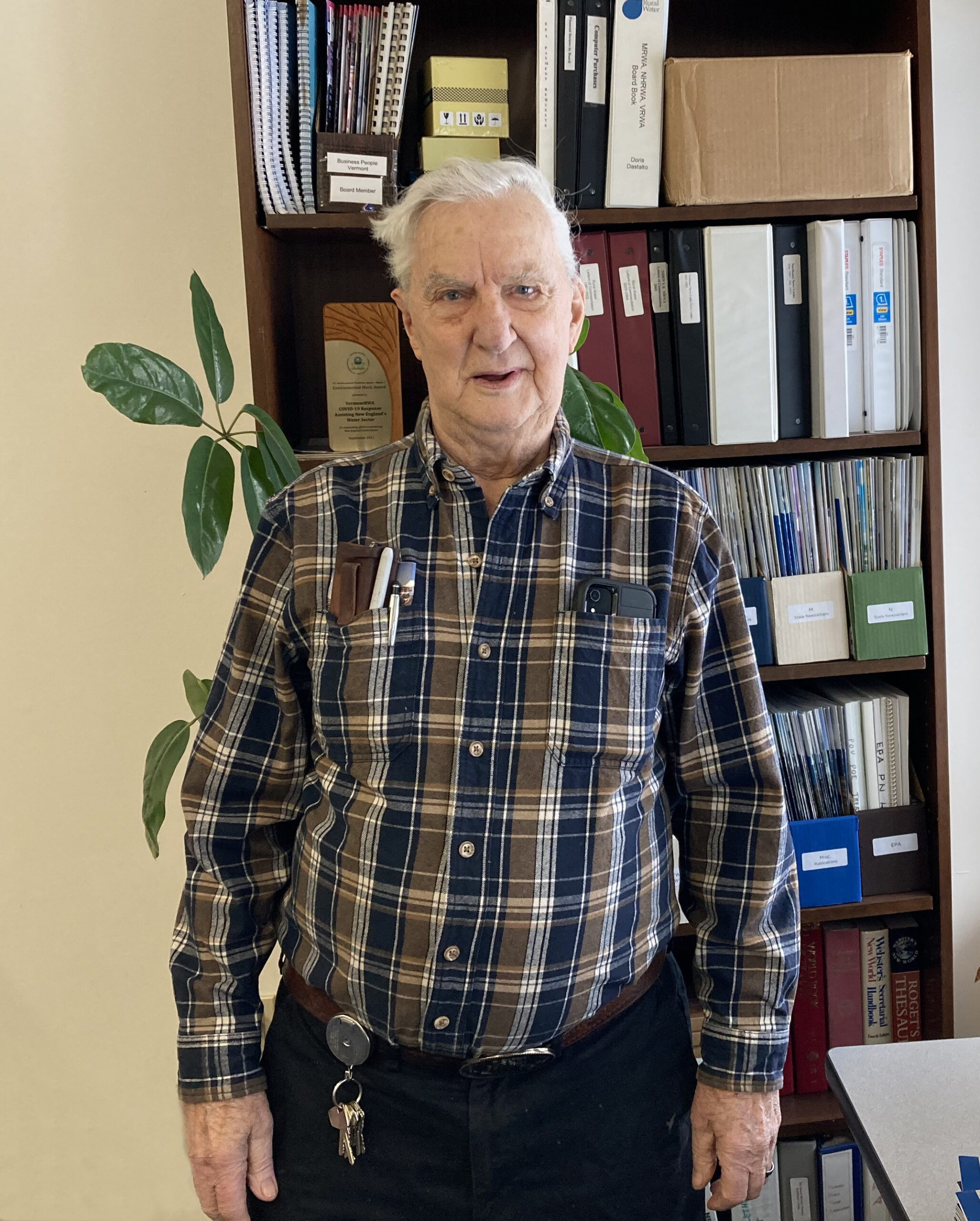 A man in a plaid shirt stands in front of a book shelf.