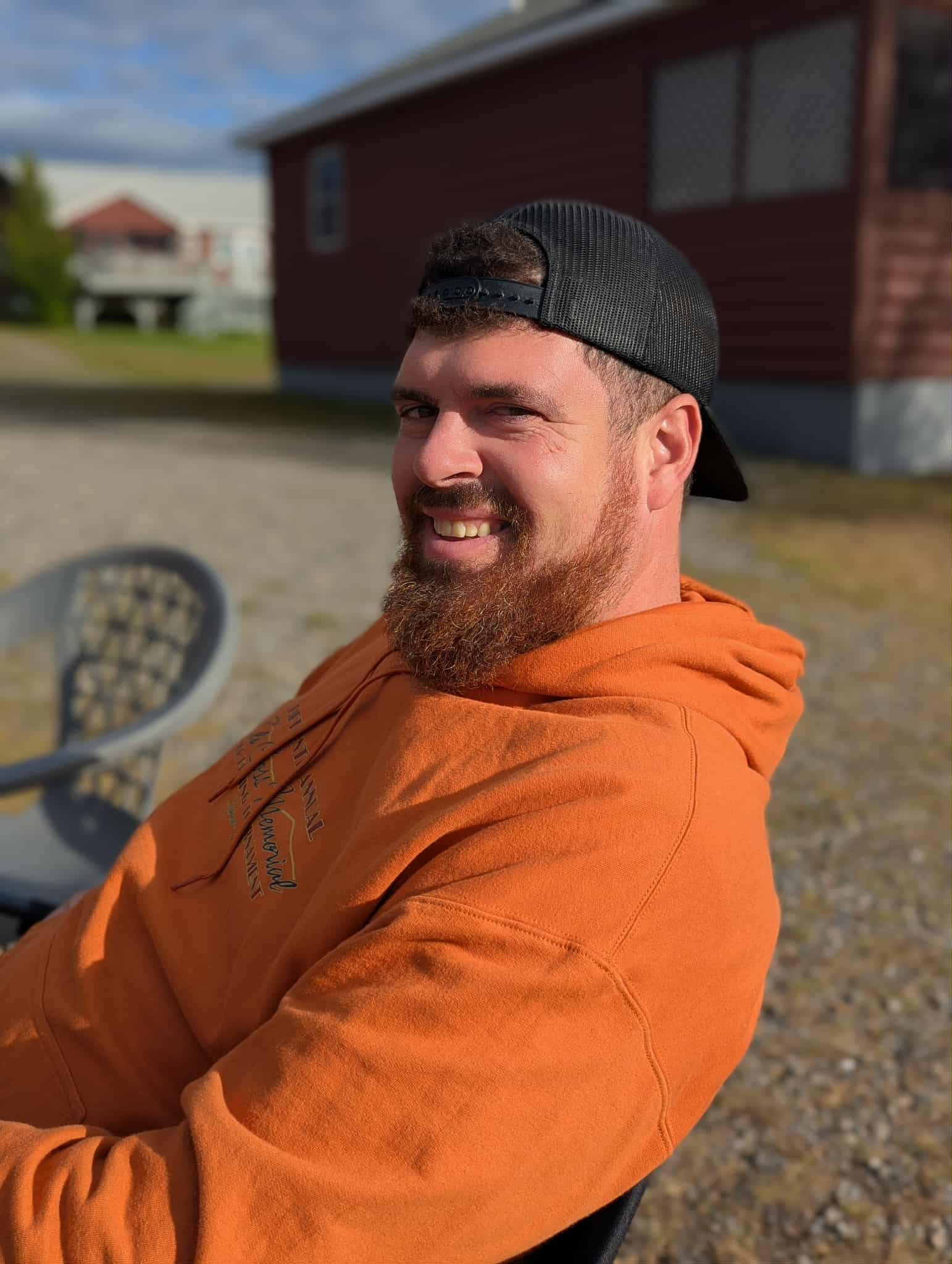 A man in a plaid shirt stands in front of a book shelf.