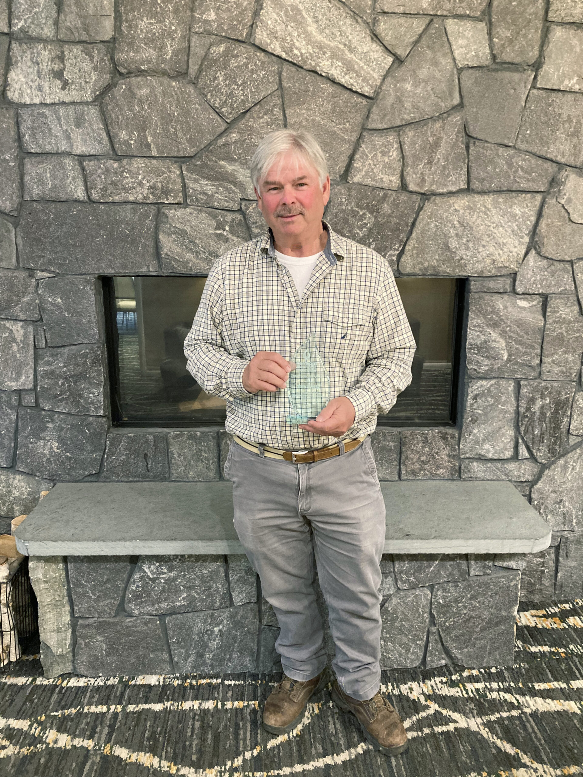 Bob Wells A man stands in front of a stone fireplace holding a glass trophy.